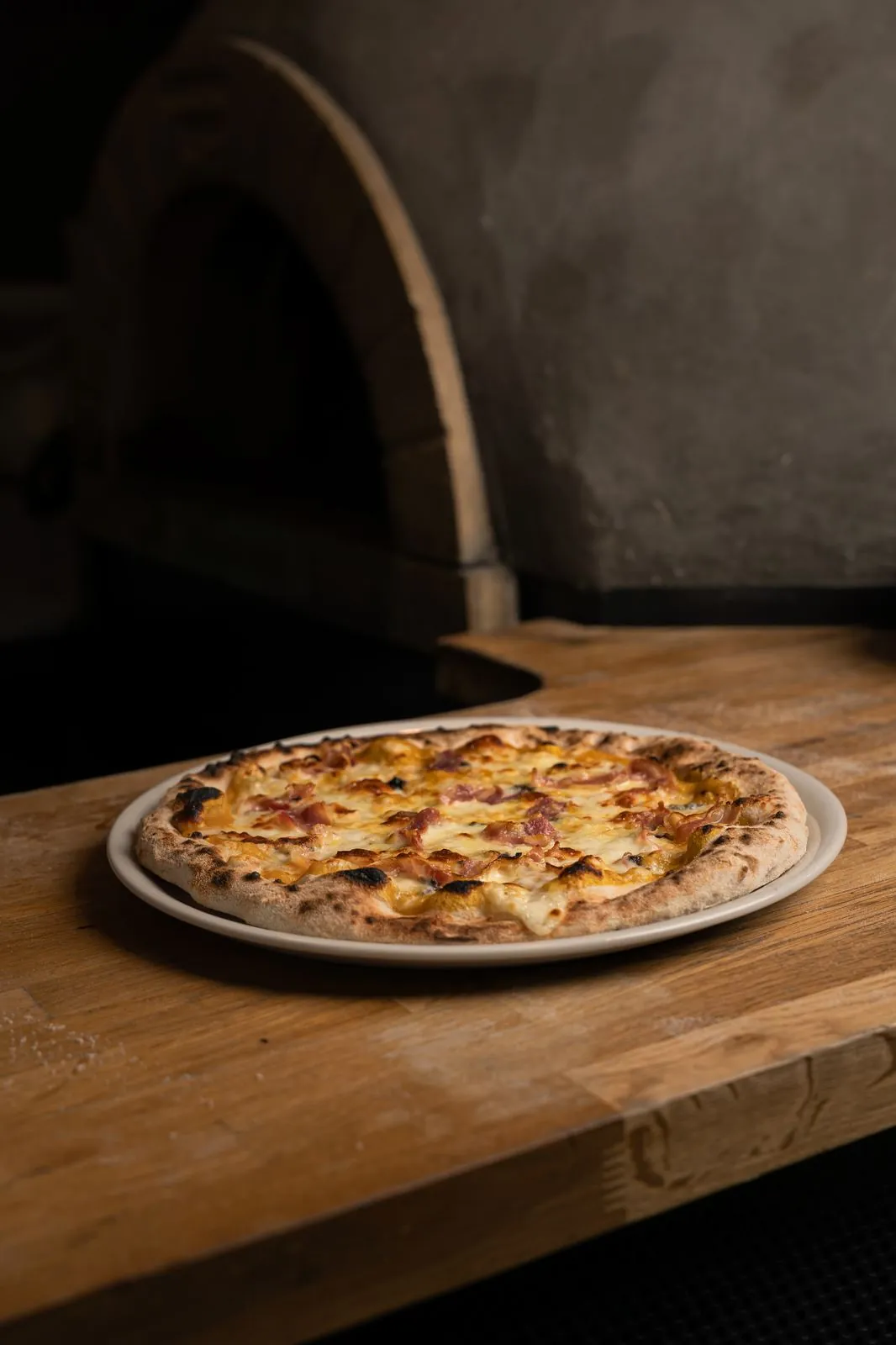 Pizza de bacon recién horneada junto al horno de piedra